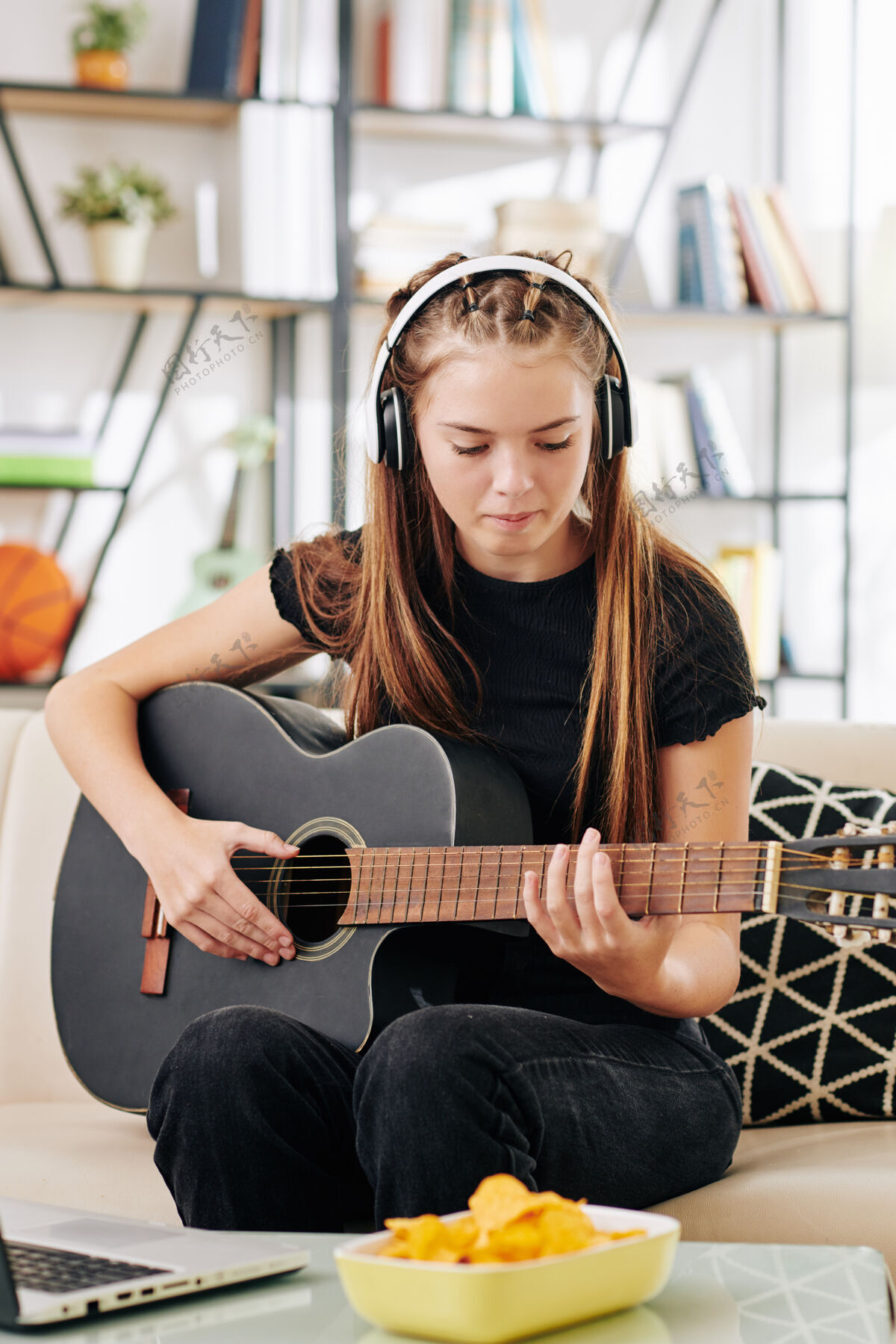 音乐天才创意少女戴着耳机坐在沙发上打开笔记本电脑前弹吉他技术声音微笑