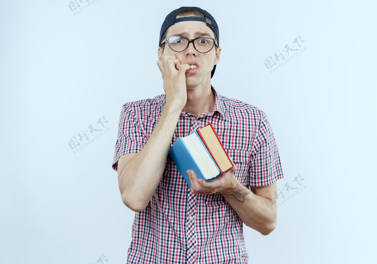 男孩关心的年轻学生男孩戴着背袋和眼镜和帽子拿着书和咬指甲抱眼镜关心