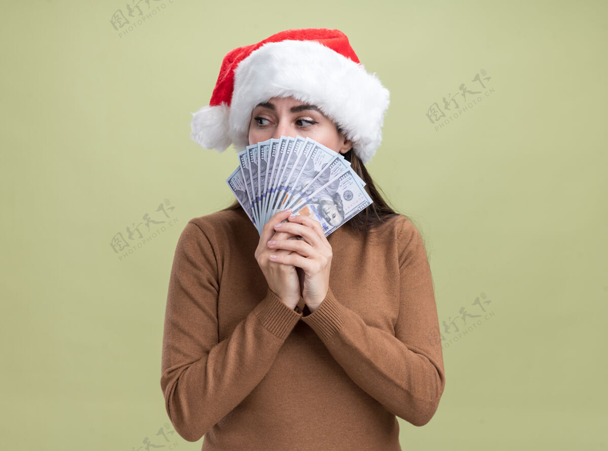 脸关切地看着身边年轻漂亮的女孩戴着圣诞帽 脸上镶着现金 背景是橄榄绿关心圣诞快乐圣诞