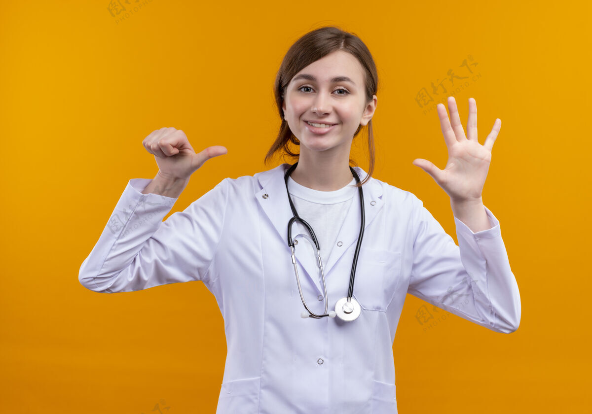 微笑微笑着的年轻女医生穿着医用长袍和听诊器 在孤立的橙色墙上显示六个女人穿长袍