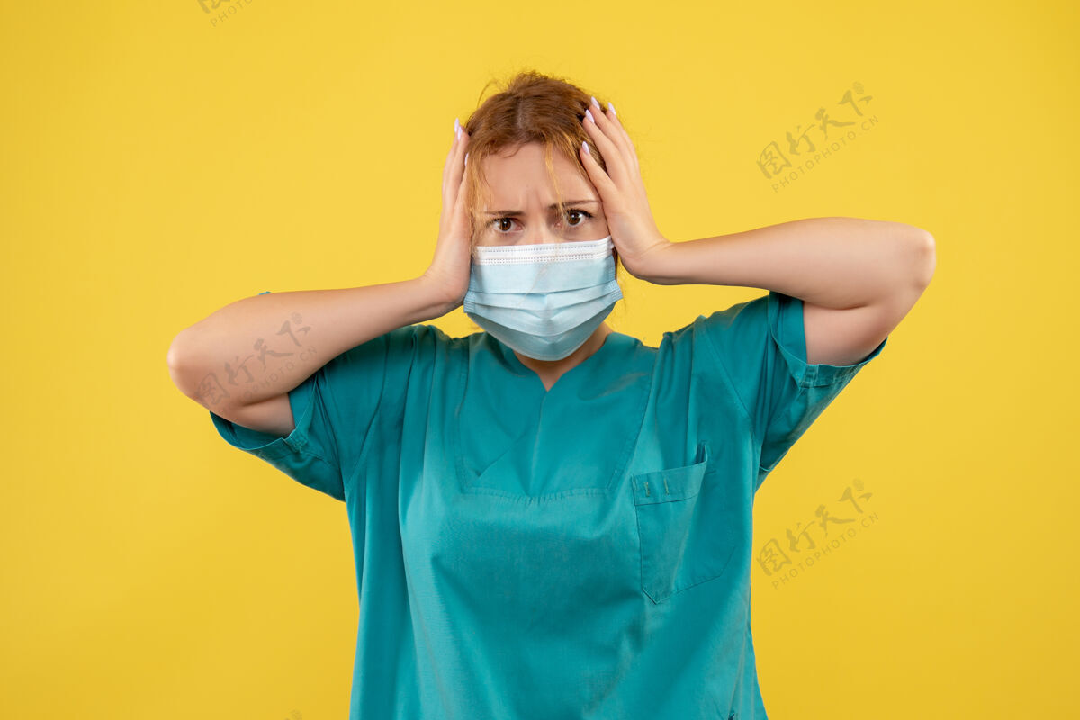 男人黄墙上年轻女医生穿着医疗服 戴着口罩的正面图人成人面具