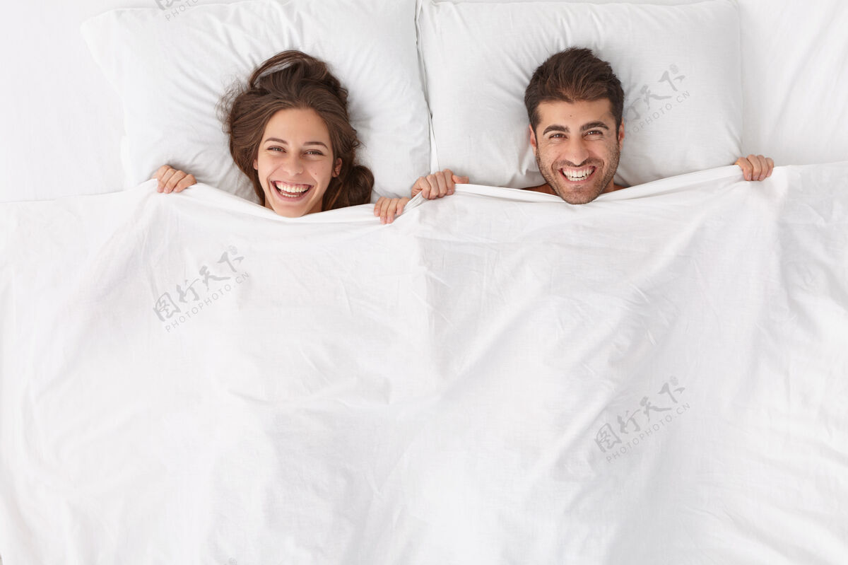 配偶快乐的夫妻享受在一起的时光 躺在白毯子下 有积极的表情和微笑 呆在床上 睡后醒来或清晨小睡 在深度健康的夜晚后感觉焕然一新 睡眠高兴头顶
