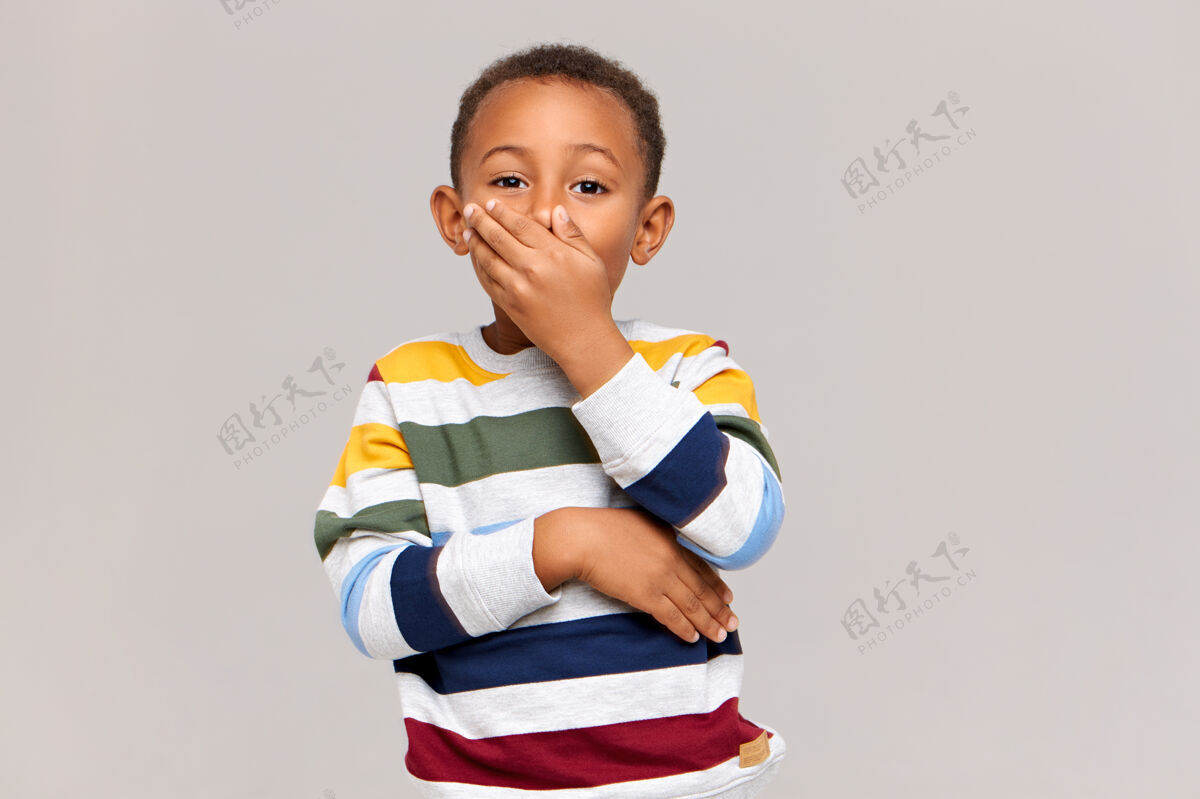 年轻情绪化的可爱的非洲裔美国男孩 表达惊讶或惊讶 用手捂住嘴表示震惊或保密 保持舌头不动真实的人类情绪和反应惊喜年轻沉默