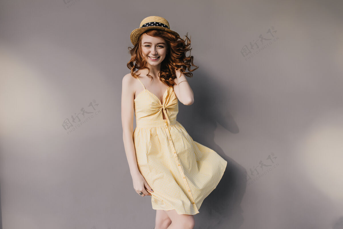 波浪在灰色墙上拍照时 戴着优雅帽子的可爱姜汁女孩微笑着穿着漂亮夏装的苗条华丽女士的室内照片情绪化配饰波浪发
