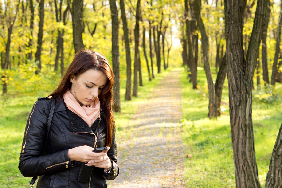 技术忧心忡忡的女人站在穿过林地的人行道上 用手机读着一条短信短信走道阅读