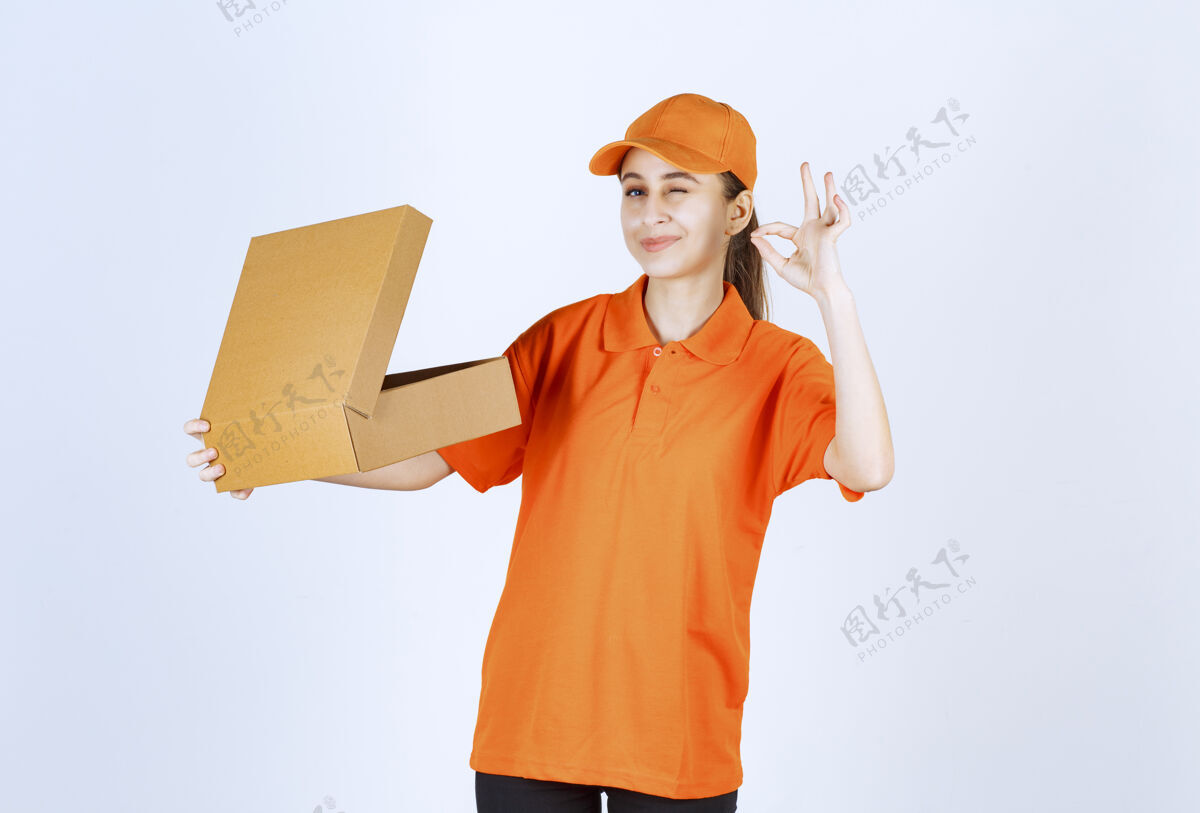 运输身着橙色制服的女快递员手持一个打开的纸板箱 并显示正面手势动力保证强壮