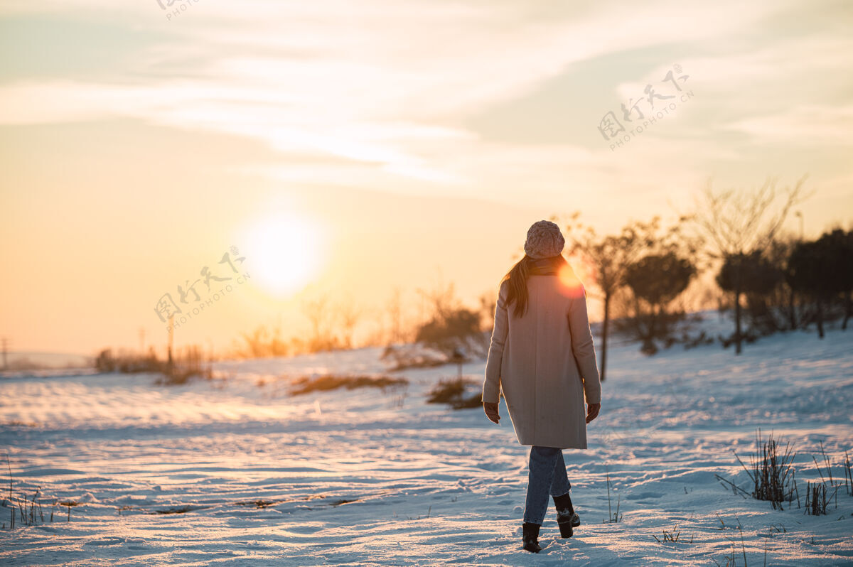 全长一个穿着暖和衣服的女人独自站在雪白的草地上 欣赏冬日乡间如画的日落阳光雪风景