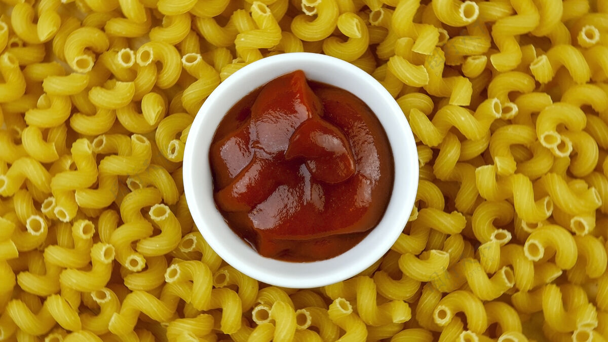 通心粉在许多螺旋形的干面食的背景上放上美味的红色番茄酱厨房营养意大利料理
