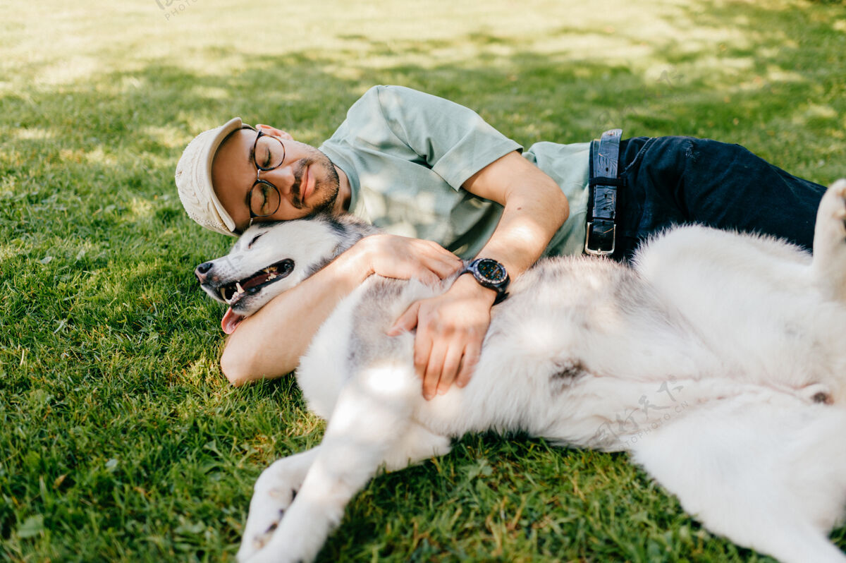 谎言一个可爱的男人和一条狗躺在草地上朋友睡眠成人