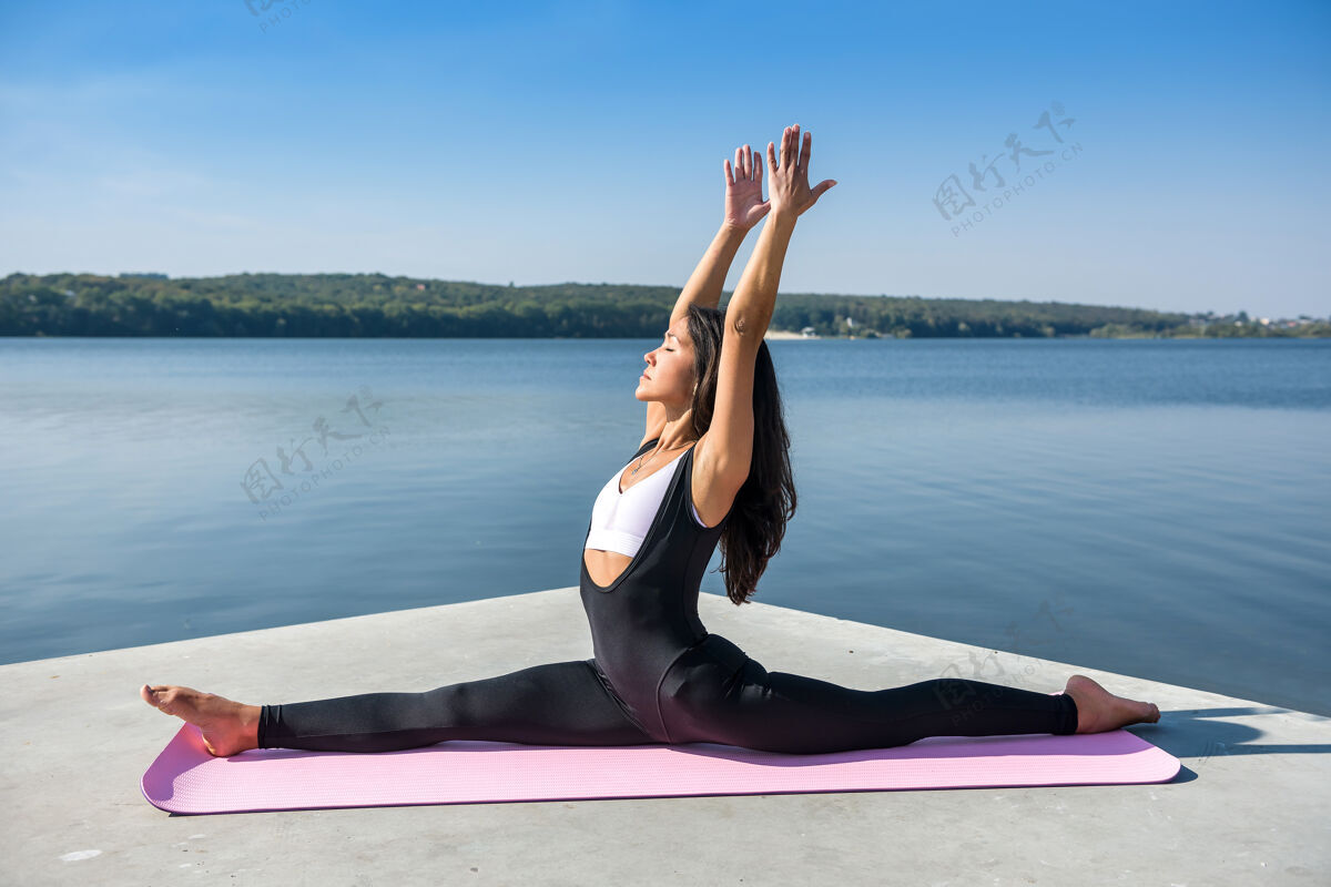 健身年轻的欧洲女运动员在湖边做伸展腿的运动 坐在外面的劈叉上健康的生活方式训练瑜伽手