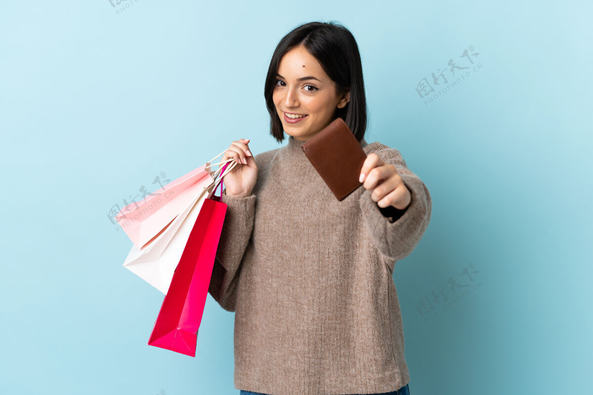 年轻人一位年轻的白人妇女 手拿购物袋和信用卡 被隔离在蓝色背景下女孩商店电子商务