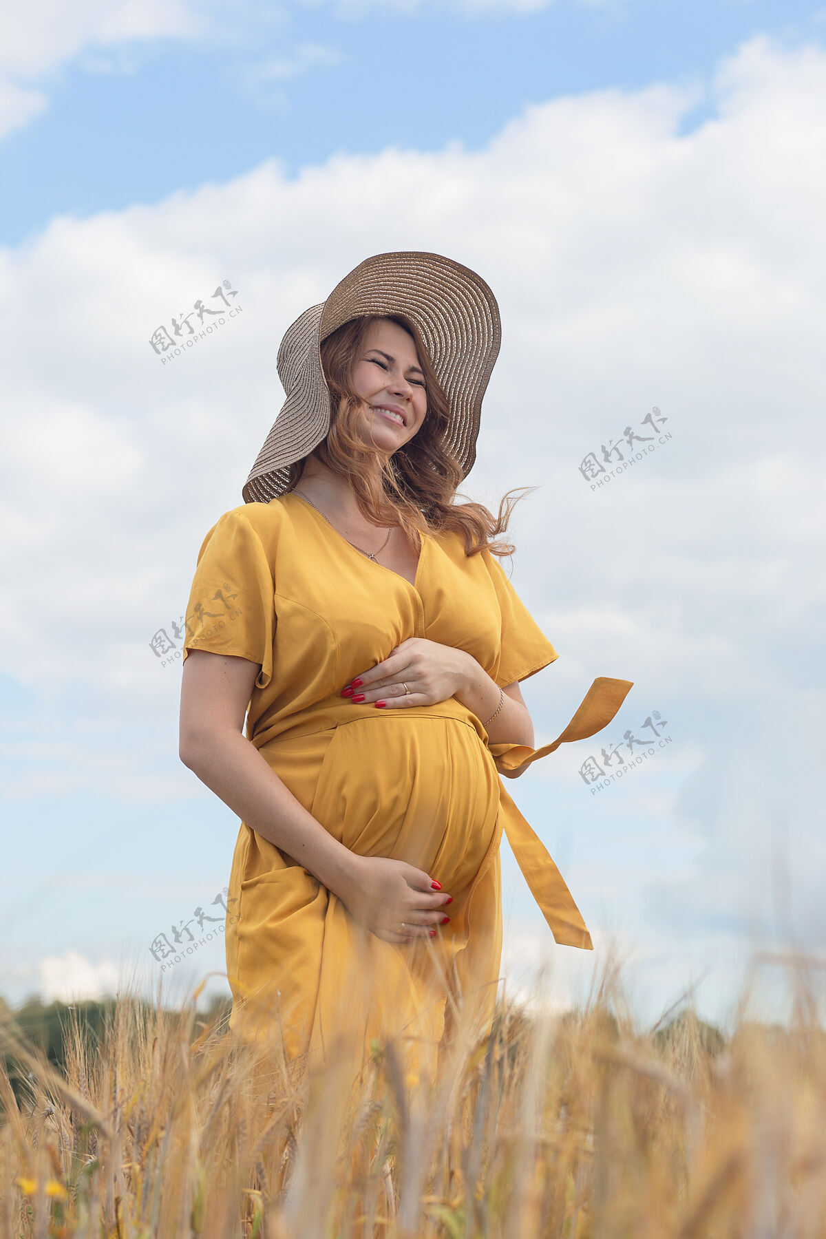 太阳在一个阳光明媚的夏日 一位年轻漂亮的孕妇穿着黄色的裙子 戴着黄色的帽子 走过一片麦田阳光可爱天空