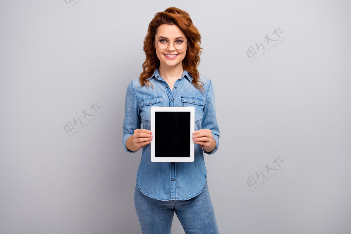 模特正面女性形象推广员手持平板电脑展示新设备广告推广员建议选择穿好看的衣服隔离在灰色墙壁上屏幕休闲时尚