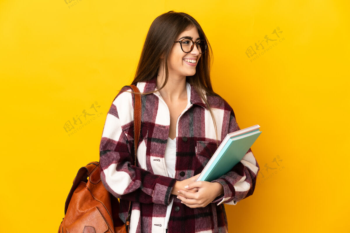 文件夹年轻的女学生孤立在黄色背景的一边看脸表情女性