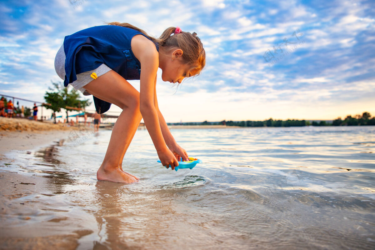 旅游侧视图：可爱的白人小女孩站在沙滩上 在蓝色的小水池里和小橡皮黄鸭子玩耍夏天海滩乐趣