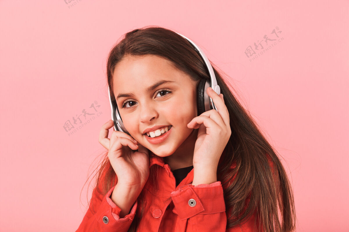 年轻画面中的白人小女孩穿着休闲的耳机听着音乐 隔着红墙孤立着年轻人快乐耳机