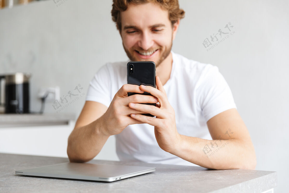 文学一个快乐的留着胡子的年轻人坐在家里的桌子旁 在笔记本电脑旁打电话室内笔记本电脑白种人