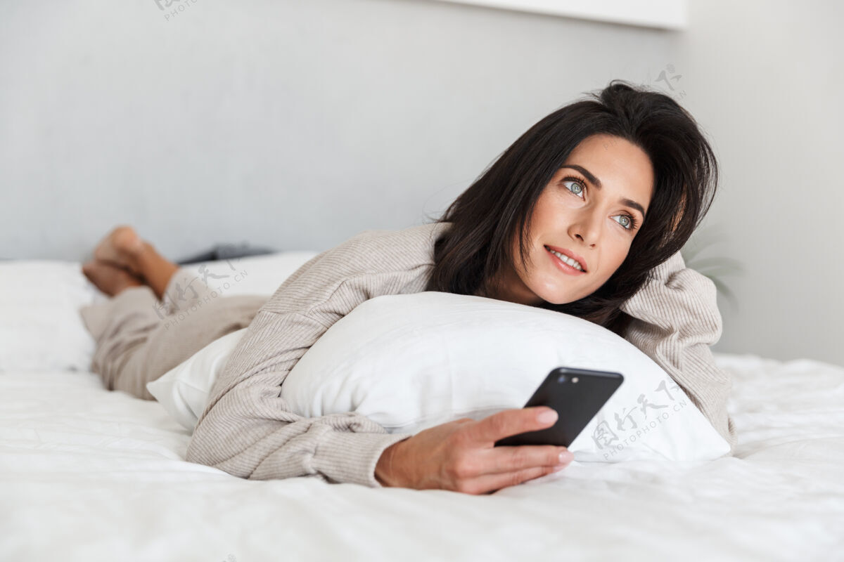 可爱一张30多岁的欧洲女人在明亮的房间里躺在床上用手机的照片谎言小玩意手机