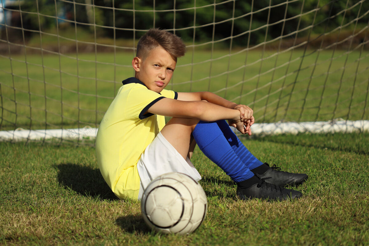 活跃穿着黄色t恤的帅哥足球运动员拿着球坐在球门附近游戏球运动