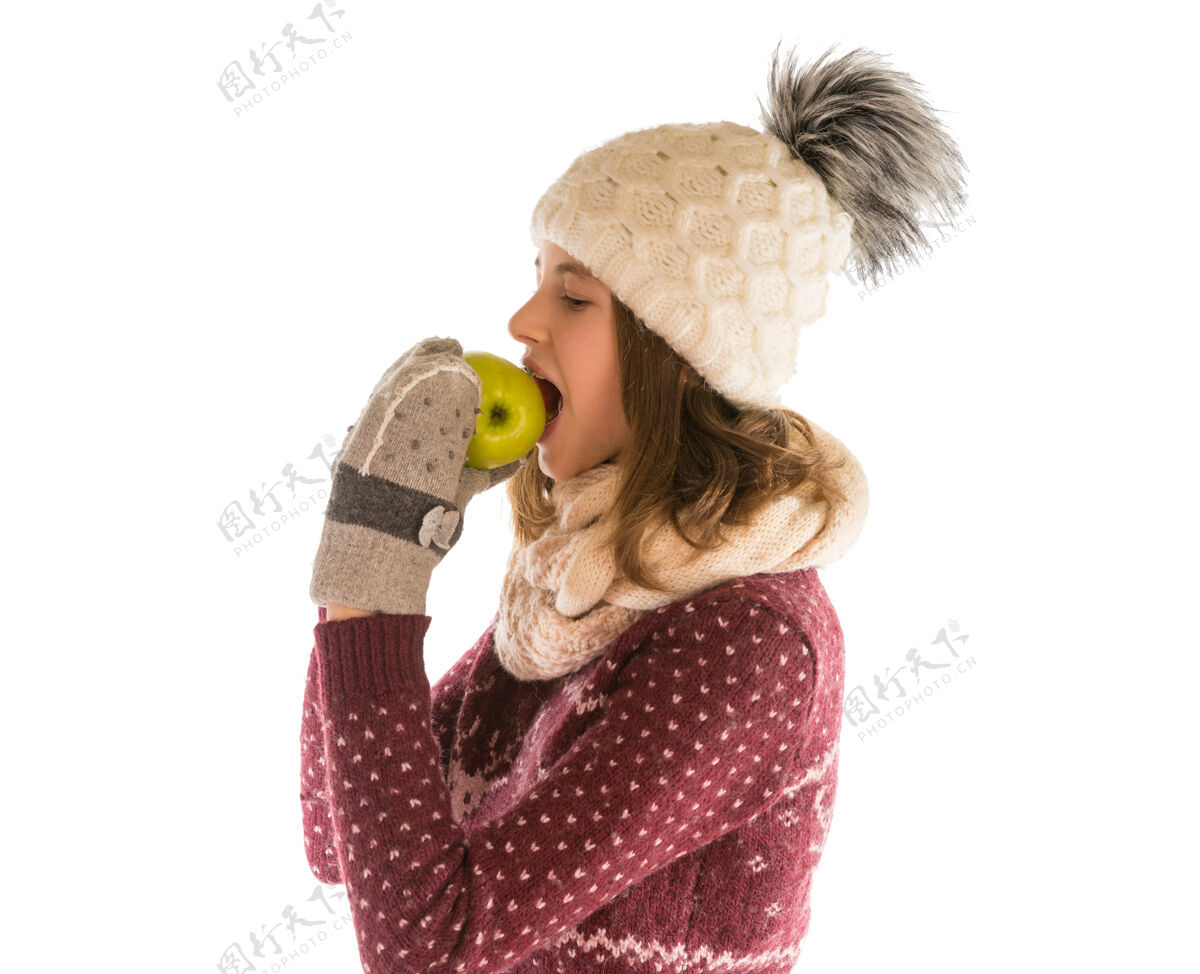 年轻可爱的女孩在温暖的毛衣 帽子 围巾和手套吃苹果隔离在白色爱苹果肖像