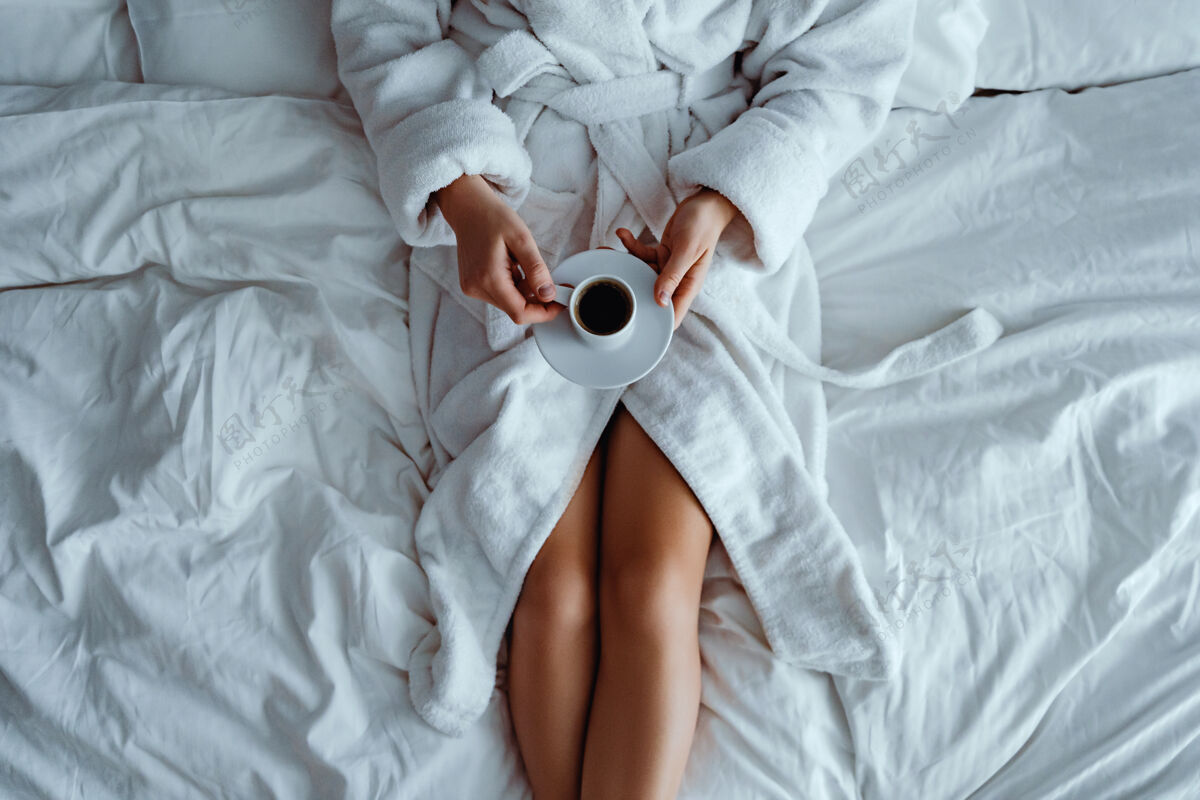 享受懒女人穿着浴衣躺在床上 享受着芳香的咖啡杯 在酒店舒适的卧室里放松房子醒来手
