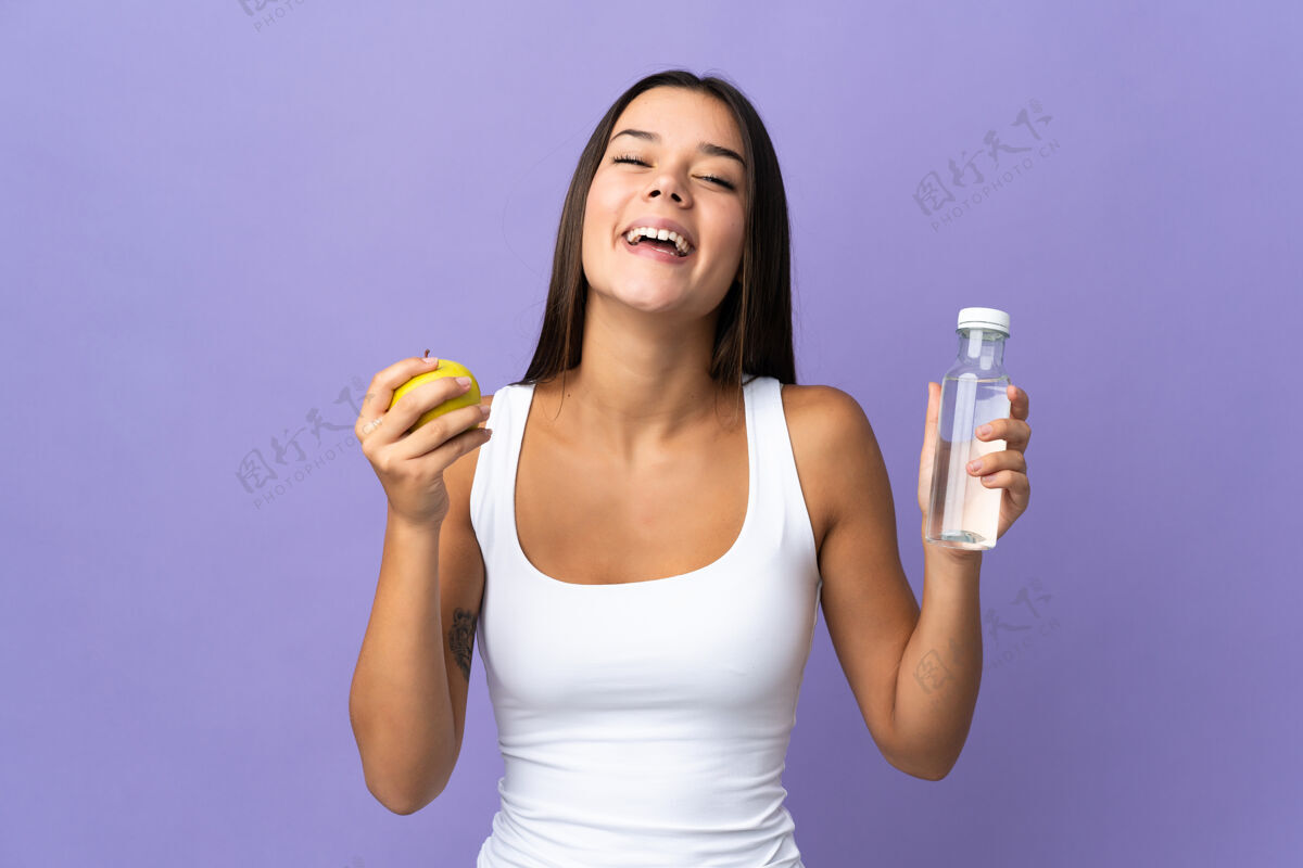 饮料一个女人用一个苹果和一瓶水隔离在紫色的土地上女人液体苹果