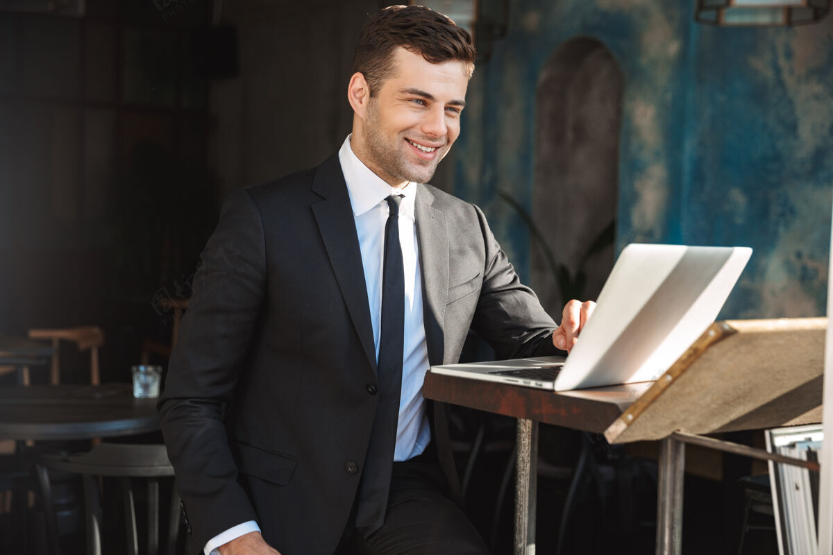男人一个英俊快乐的年轻商人坐在咖啡馆里用笔记本电脑的形象领导笔记本电脑白种人