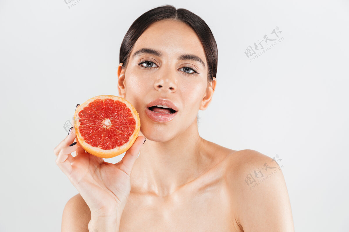魅力美丽的肖像画 一个迷人的健康的女人孤立地站在白色的墙上 摆着半个柚子化妆吸引力一半