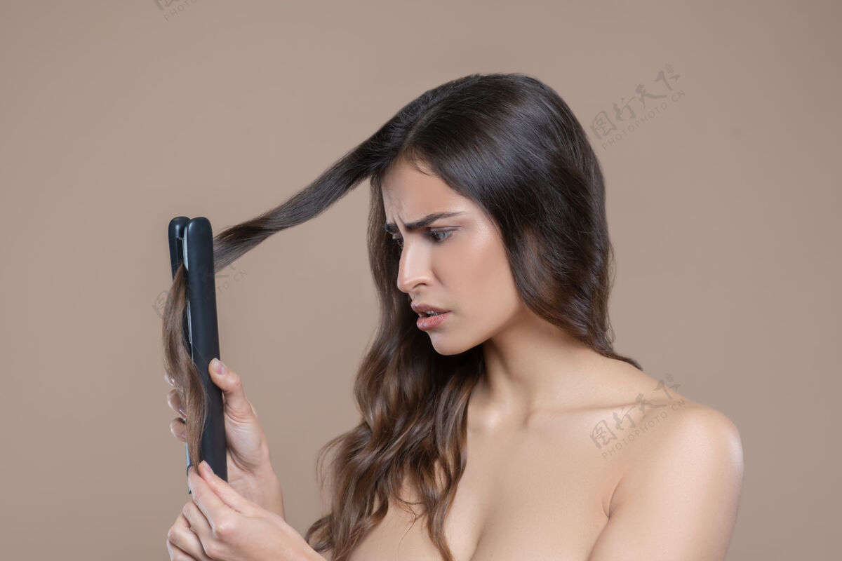 结果不满年轻的长发女人 光着肩膀 用熨斗抚平一绺头发半裸长发女人