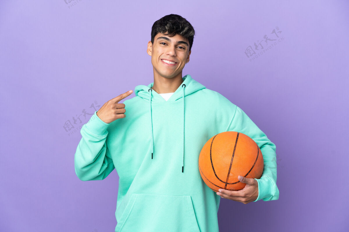 爱好年轻人在孤立的紫色墙壁上打篮球 竖起大拇指西班牙裔运动装自豪