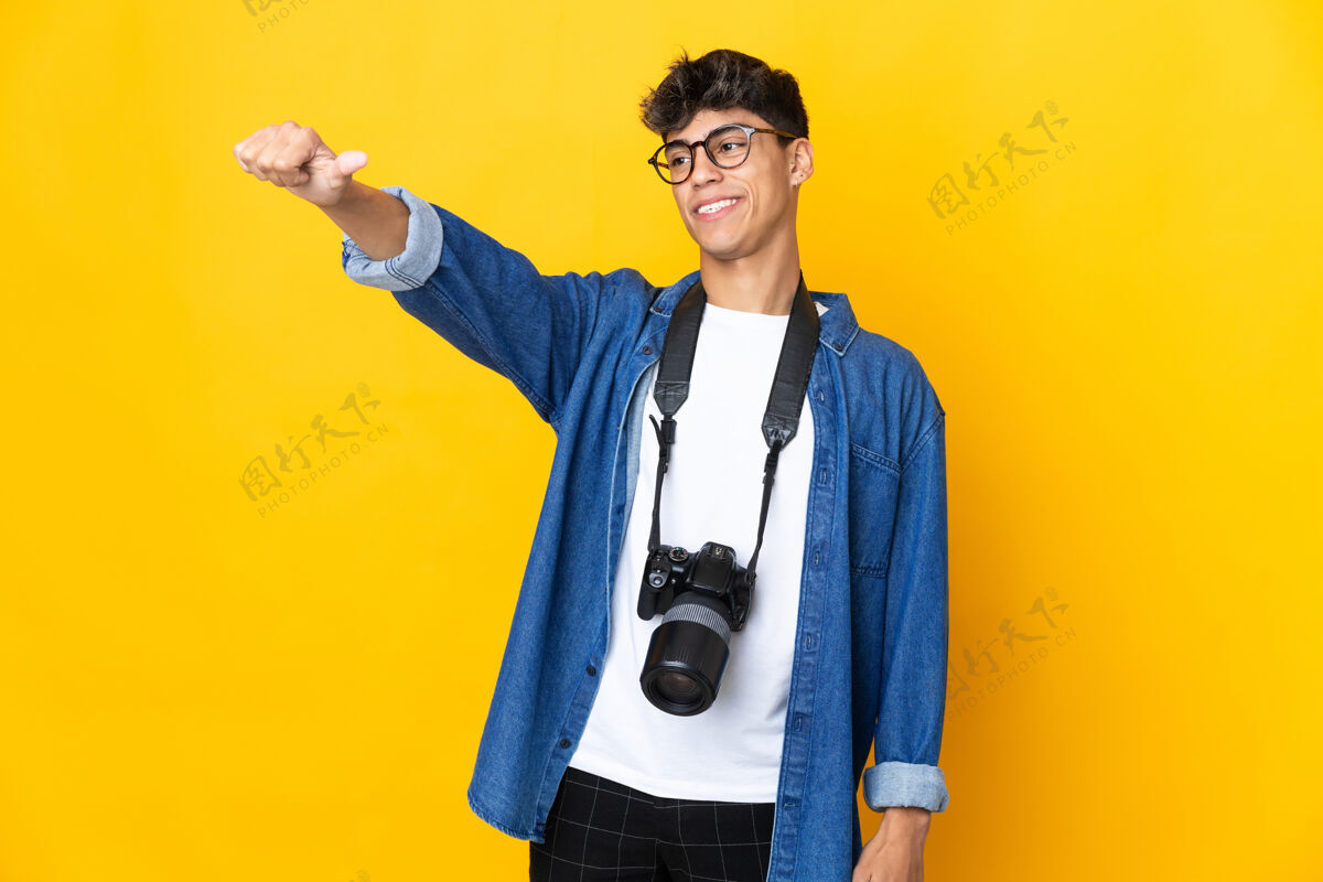西班牙裔年轻的摄影师越过隔离的黄色墙壁 竖起大拇指微笑年轻男人