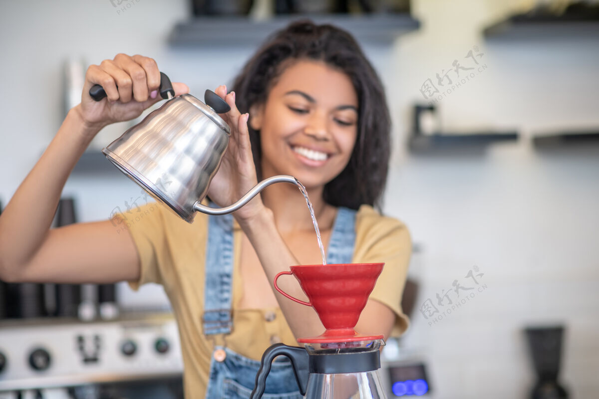 长发工作 浓缩咖啡师年轻快乐的女人 留着长长的黑发 心情愉快地用滴头煮咖啡暗色工作腰向上