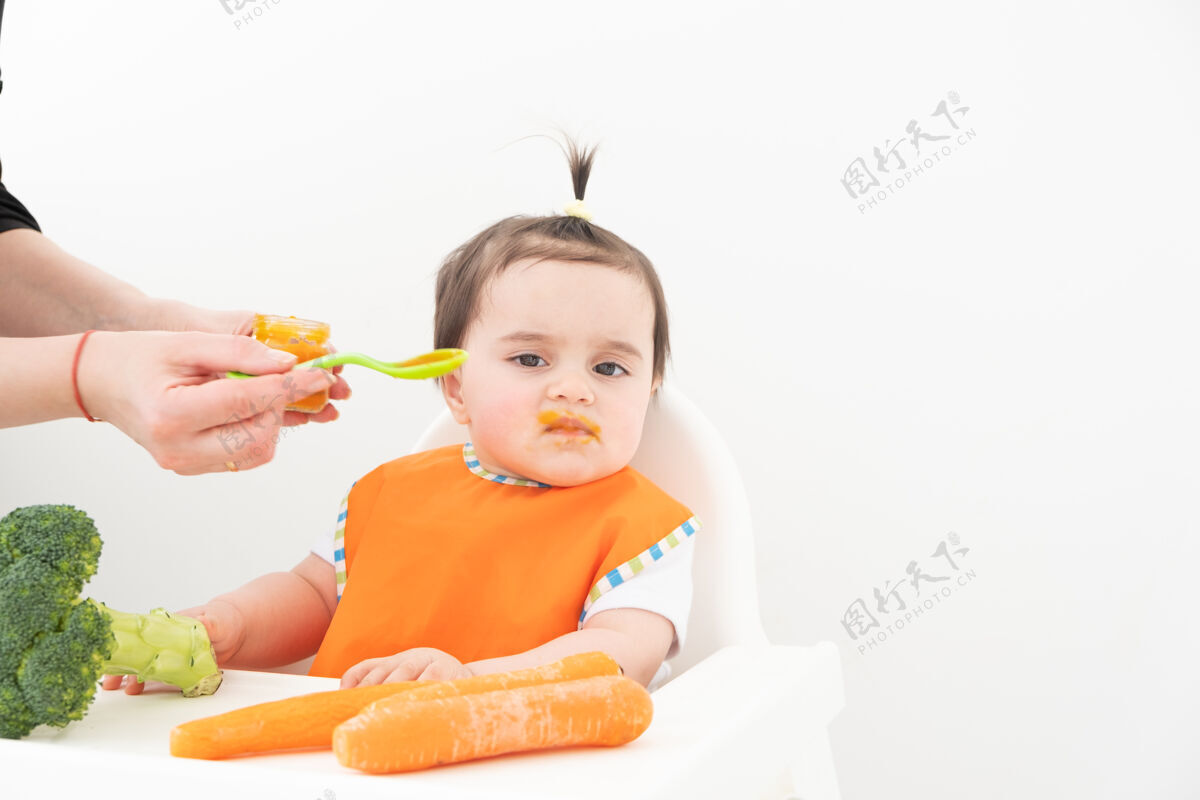 食物坐在儿童椅上吃白色蔬菜泥的女婴婴儿妈妈手