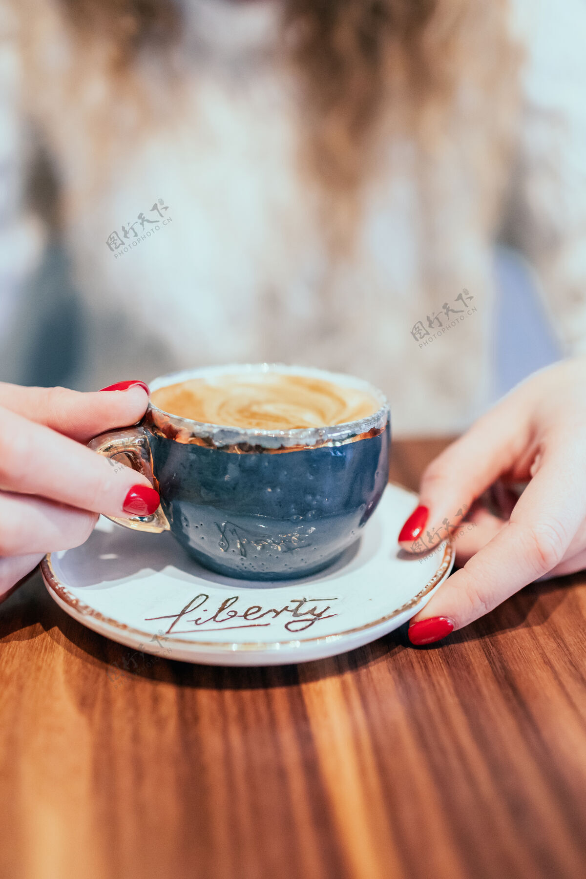 指甲美丽的女性双手捧着一杯灰色的咖啡卡布奇诺桌子木头手