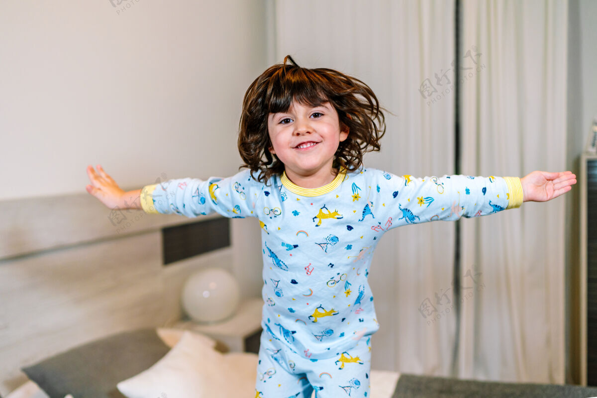团结睡前穿着睡衣 张开双臂跳在床上的孩子非常开心可爱天真幼儿园