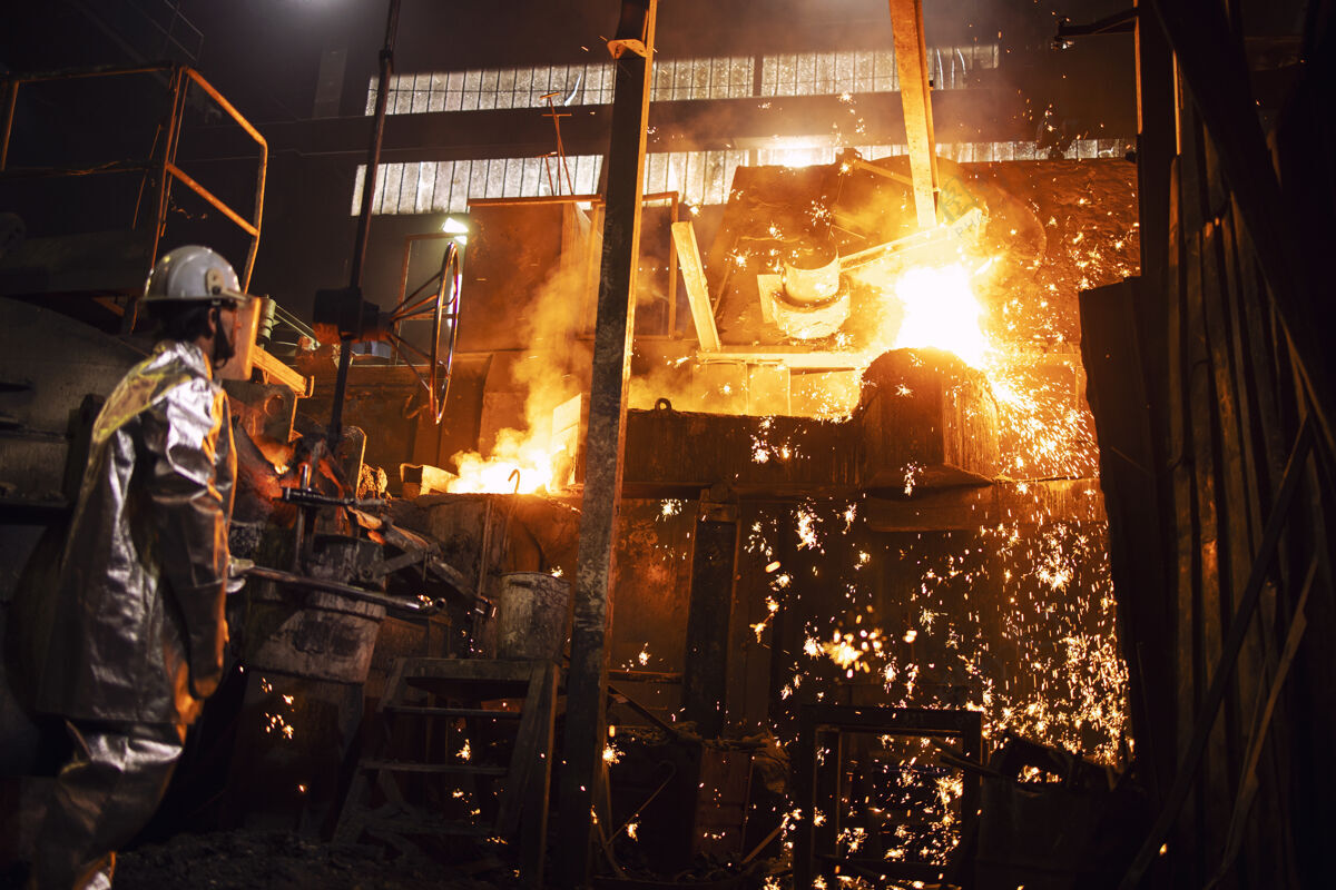 人员穿着镀铝防护服的工人站在热铁水和火花飞溅的熔炉旁 从事铸造和工业钢生产工人工业金属