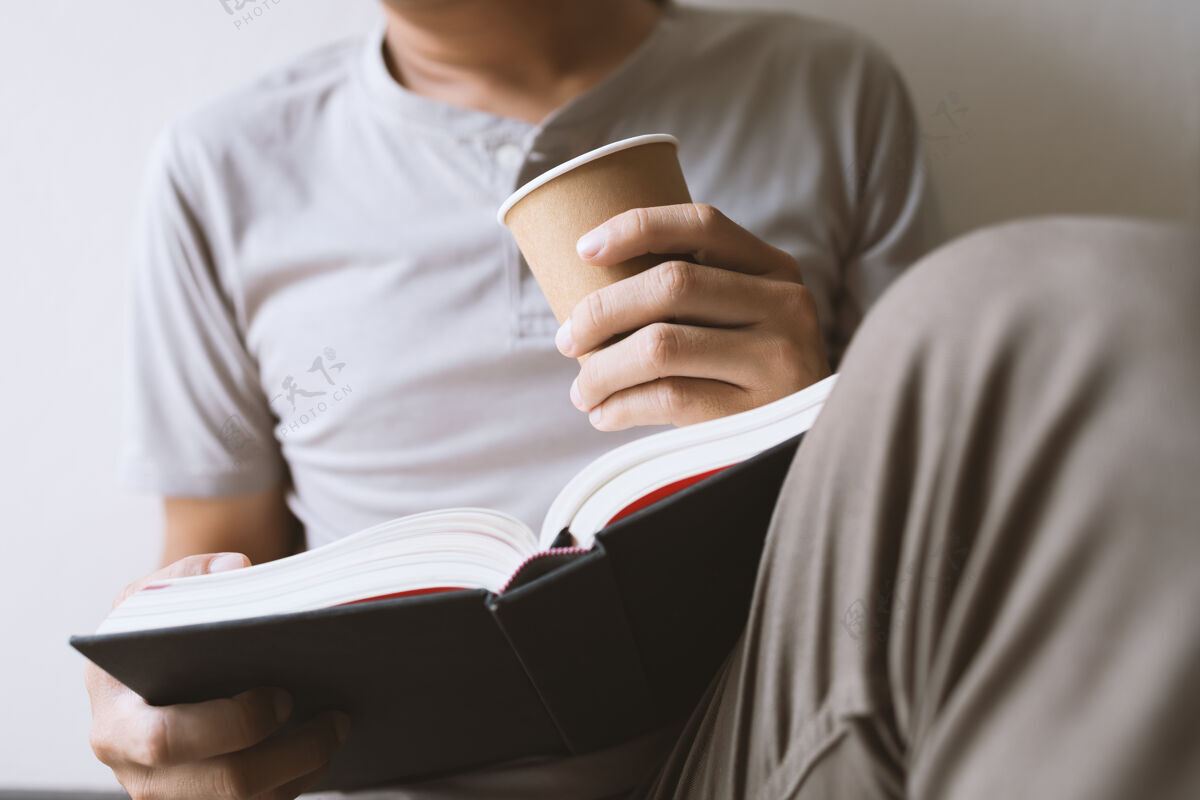 纸张年轻人坐在房间里看书 手里拿着一杯咖啡 背景是柔和的焦点和光线教育成人窗户