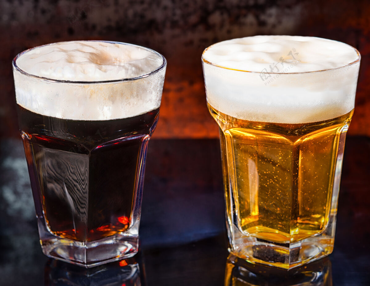 滴在黑镜子上放两杯新倒的黑啤酒和淡啤酒表面.食品和饮料概念透明冷冻酒精