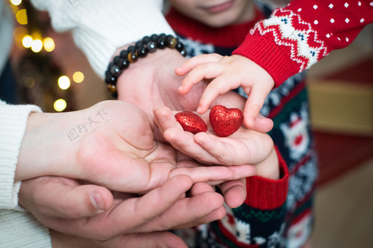 情侣女性 婴儿和男性的手都握着两个红色的 闪闪发光的红心情人节情人节 爱 支持 信任白天男朋友情人节