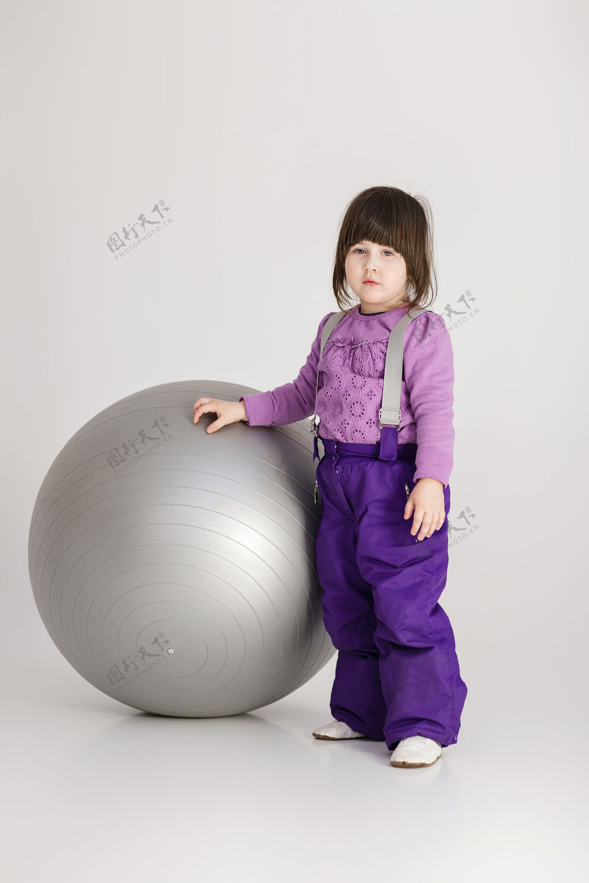 玩具穿着紫色衣服的可爱小女孩 灰色背景上有一个健身用的大球紫色美丽无忧无虑