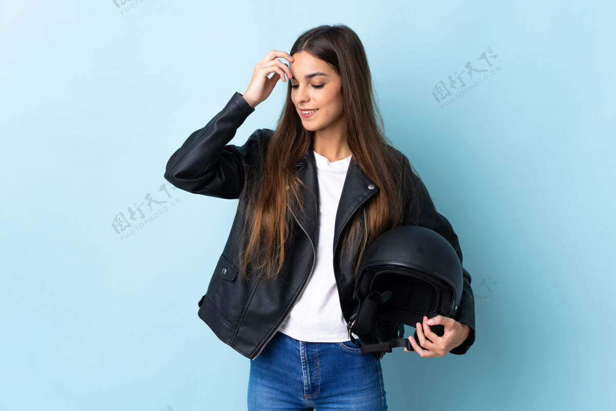 微笑年轻的高加索女子手持摩托车头盔孤立在蓝色背景笑皮革年轻大笑