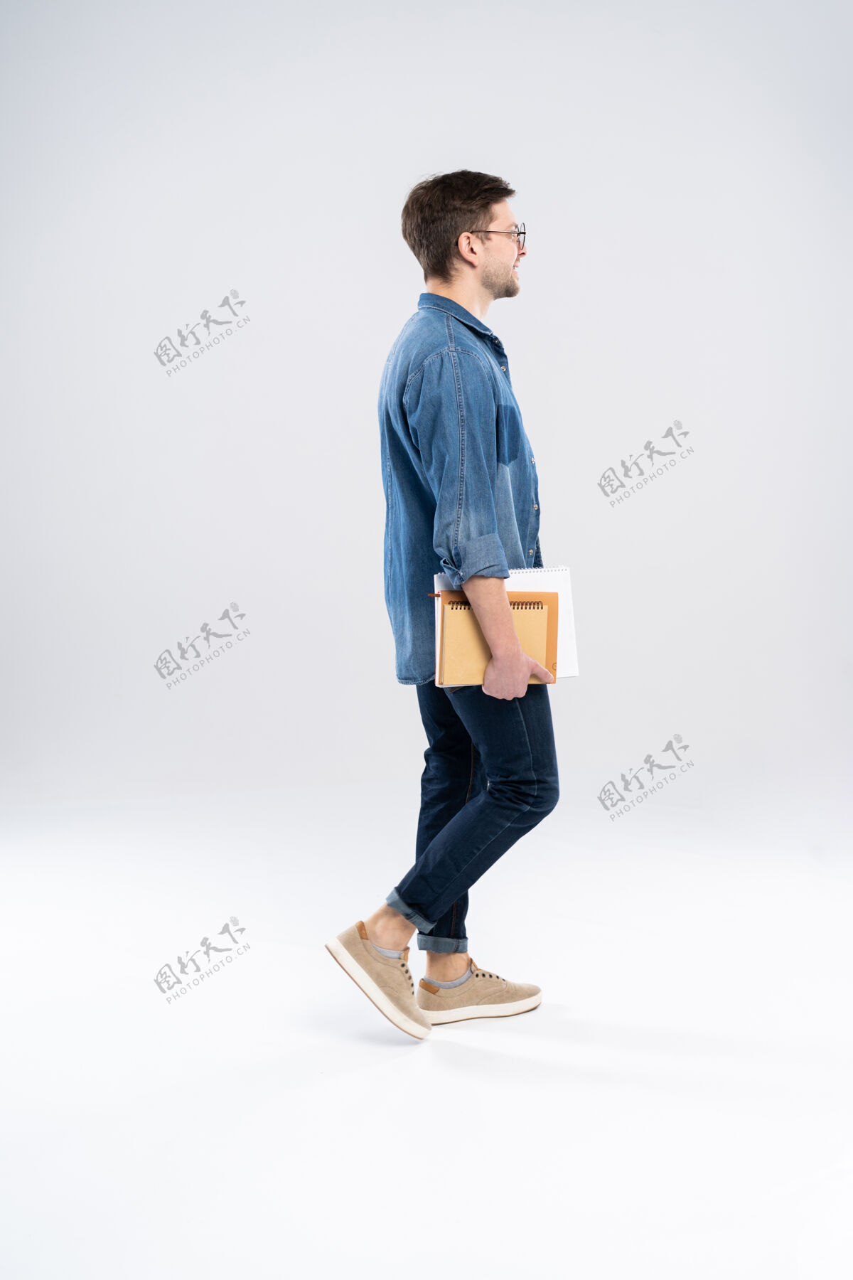 侧线侧视图：一个面带微笑的年轻人走着 学生拿着书和笔记可爱站立向前