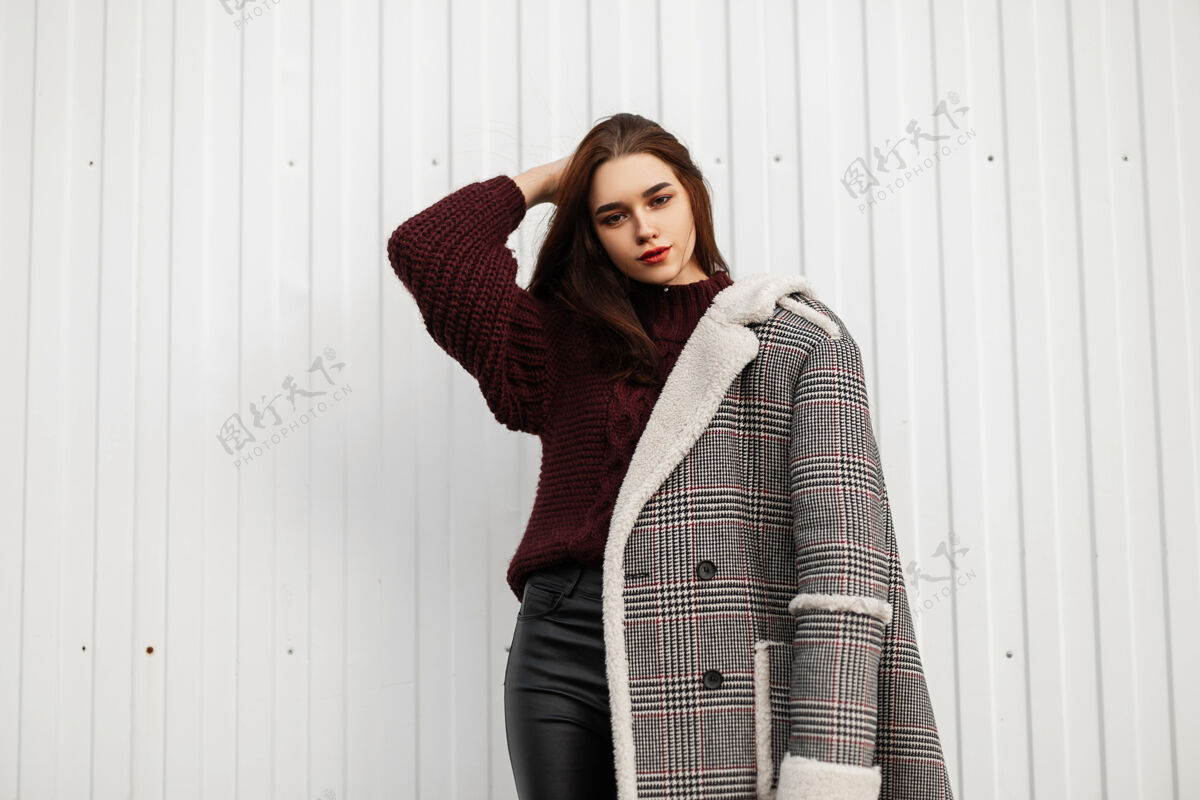 年轻人漂亮的年轻女子穿着时髦的格子皮草长夹克姿势建筑外套