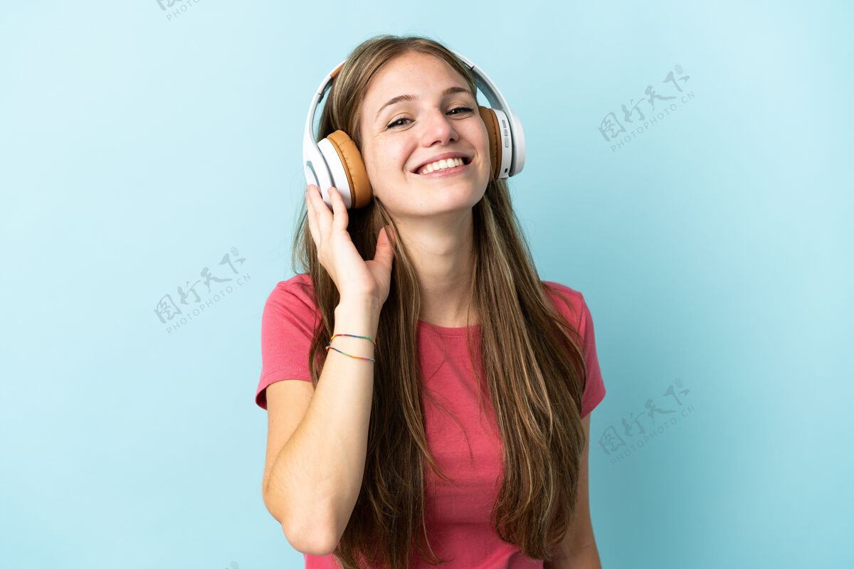 聆听年轻的白人妇女在蓝色背景下听音乐成人快乐耳机