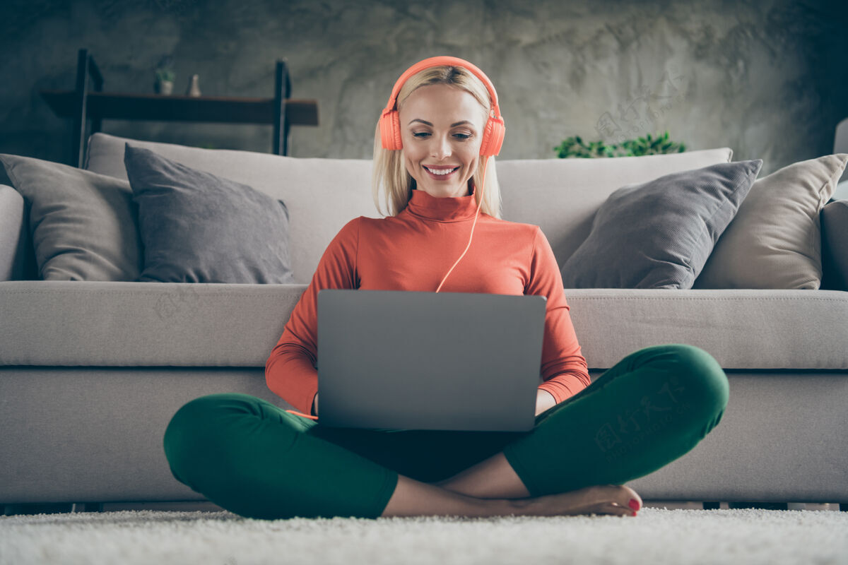 电影照片中的美女抱着笔记本跪在地上自由职业者听音乐现代科技耳罩坐在地毯地板上靠沙发休闲装室内互联网听电脑