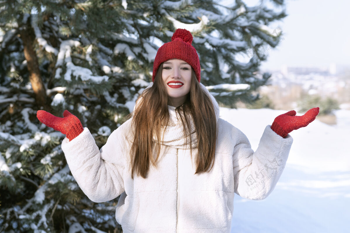 户外快乐美丽的黑发女孩戴着红帽子和布波在雪林阳光帽子乐趣