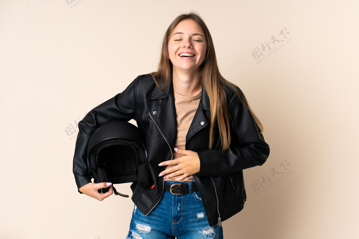 骄傲立陶宛年轻女子手持摩托车头盔孤立在米色背景笑了很多金发女性肖像