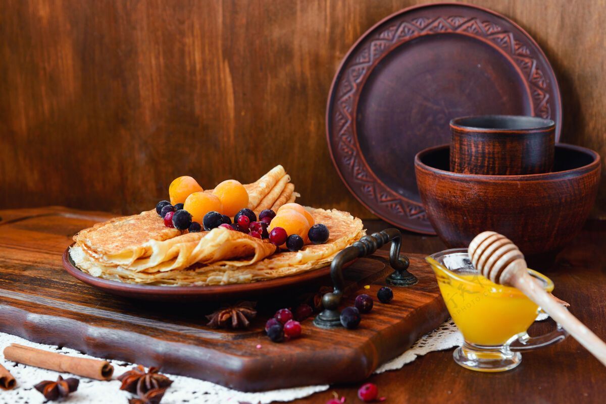 俄罗斯金煎饼 冷冻水果 装饰和蜂蜜在一个乡村风格圆的烘焙午餐