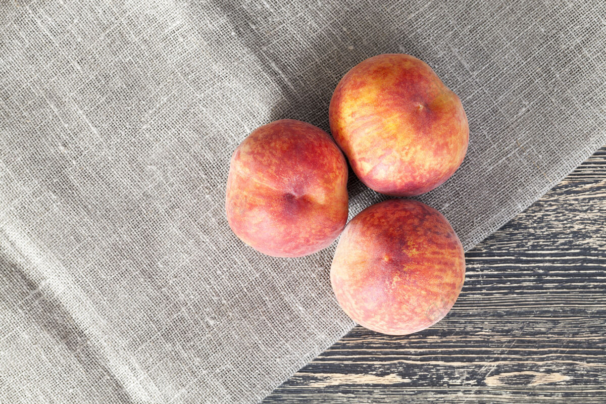 营养木桌上放着三个桃子和一张亚麻餐巾桃甜食水果