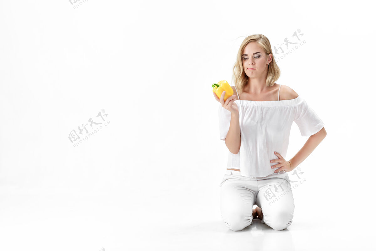 体重穿着白色上衣的漂亮严肃的金发女人看着黄色的铃铛胡椒粉健康吃和节食健康有机年轻